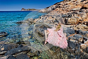 Beautiful blond woman pink ballroom dress standing on the rocks in Santorini