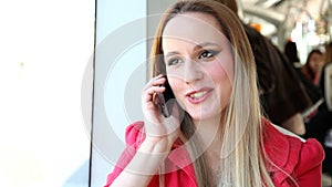 Beautiful blond woman sitting in tram, answering phone, looking surprised