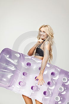 Beautiful blond woman in swimsuit holds an air mattress on white isolated at hand, applies a finger to her mouth