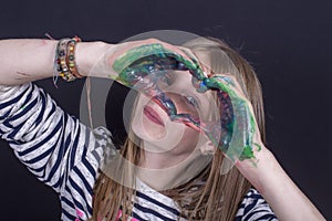 Beautiful blond young girl with freckles and hands painted in colorful paints indoors on black background, closeup portrait