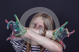 Beautiful blond young girl with freckles and hands painted in colorful paints indoors on black background, closeup portrait