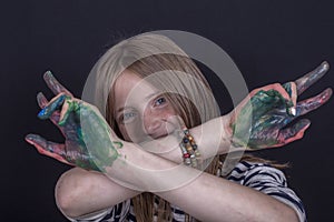 Beautiful blond young girl with freckles and hands painted in colorful paints indoors on black background, closeup portrait