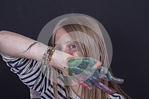 Beautiful blond young girl with freckles and hands painted in colorful paints indoors on black background, close up portrait