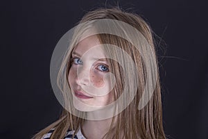 Beautiful blond young girl with freckles indoors on black background, closeup portrait