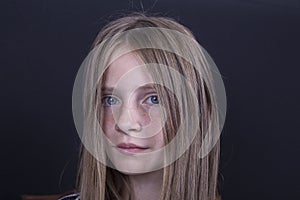 Beautiful blond young girl with freckles indoors on black background, closeup portrait