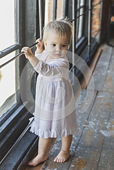 Beautiful blonde baby in a nightgown near the window