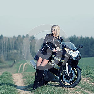 Beautiful blonde with a biker posing near a sports bike.