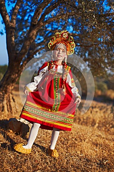 Beautiful blonde braided girl in Russian folk costume dancing under tree