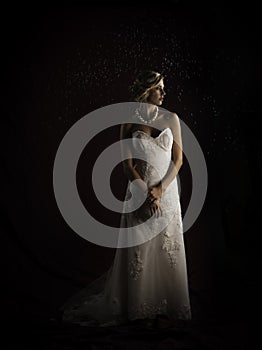 Beautiful blonde bride wearing vintage strapless wedding gown standing in the rain