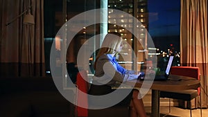 Beautiful blonde business woman working overtime at night in executive office. City lights are visible in background