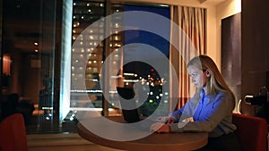 Beautiful blonde business woman working overtime at night in executive office. City lights are visible in background