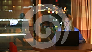 Beautiful blonde business woman working overtime at night in executive office. City lights are visible in background