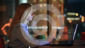 Beautiful blonde business woman working overtime at night in executive office. City lights are visible in background