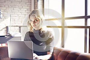 Beautiful blonde businesswoman sitting in sunny office working on laptop. Concept of young people working mobile devices.