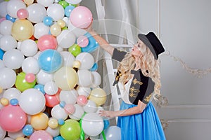 A beautiful blonde in a carnival costume decorates the tree of balloons. Charming young woman in a curvy blue skirt.
