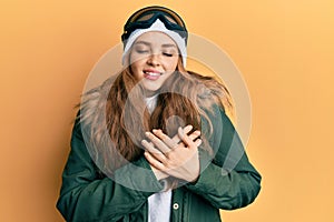 Beautiful blonde caucasian woman wearing snow wear and sky glasses smiling with hands on chest with closed eyes and grateful