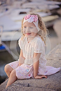 Beautiful blonde child girl portrait on sea side with boats on background