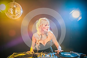 Beautiful blonde DJ girl in a white suit on decks on the party on the black background