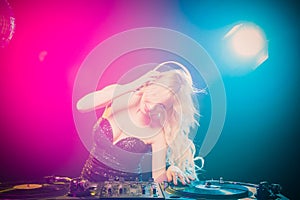 Beautiful blonde DJ girl in a white suit on decks on the party on the black background