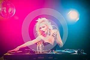 Beautiful blonde DJ girl in a white suit on decks on the party on the black background