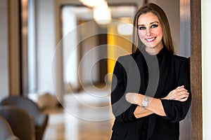 Beautiful blonde female business woman CEO in a suit at the office workplace, standing confidently with arms folded