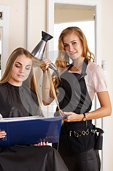 Beautiful blonde female hairdresser holding comb and hairdryer