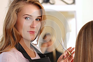 Beautiful blonde female hairdresser holding scissors