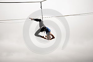 Beautiful blonde girl balancing high on a slackline against the grey sky and town