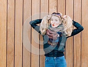 Beautiful blonde girl in black jacket posing nex to wooden wall on a sunny day and playing with her hair