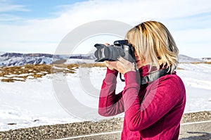 Beautiful blonde girl with a camera to take pictures of Caucasian mountains