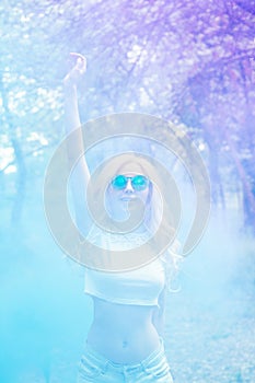 Beautiful blonde girl dancing in a multi-colored smoke outdoors in the forest. blue purple smoke. Portrait. The concept of leisure