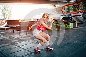 Beautiful blonde girl is doing some tricks during rollerblading. She is standing in a squat position and looking down