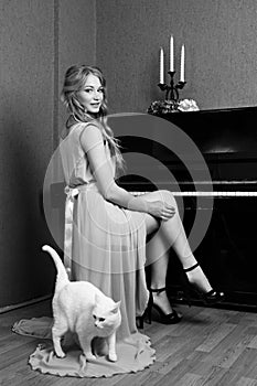 beautiful blonde girl in dress playing piano with a cat