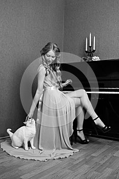 beautiful blonde girl in dress playing piano with a cat