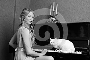 beautiful blonde girl in dress playing piano with a cat