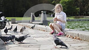 Beautiful blonde girl feeding birds in the park by the lake.