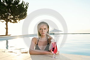 Beautiful Blonde girl with fresh juice in luxury pool