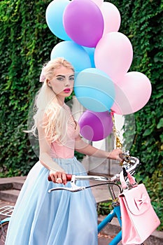 Beautiful blonde girl holding bright balloons while cycling