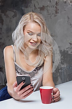 Beautiful blonde girl in home clothes is using a smartphone
