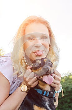 A beautiful blonde girl in a light dress and a cute dog have fun together and show their tongues.  Vertical view