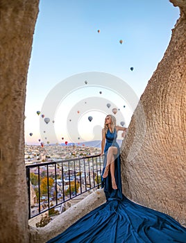 Beautiful blonde girl in the long blue dress in Cappadocia sunrise on the amazing background of hundred flying balloons