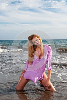 beautiful blonde girl with long curly hair on a beach with a pink dress and a white t - shirt. sexy model posing in the water of