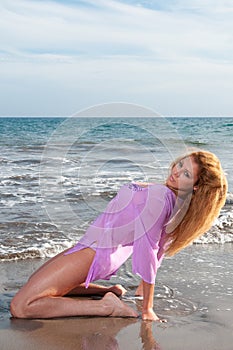 beautiful blonde girl with long curly hair on a beach with a pink dress and a white t - shirt. sexy model posing in the water of