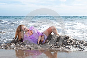 beautiful blonde girl with long curly hair on a beach with a pink dress and a white t - shirt. sexy model posing in the water of