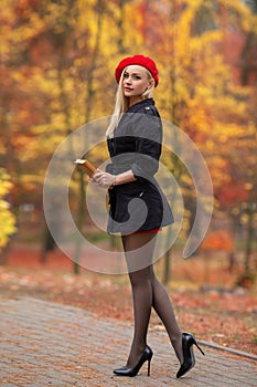 Beautiful blonde girl with perfect legs and red beret posing outdoor on the street of autumn park. Modern Little Red Riding Hood