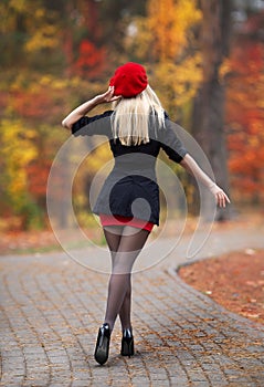 Beautiful blonde girl with perfect legs and red beret posing outdoor on the street of autumn park. Modern Little Red Riding Hood