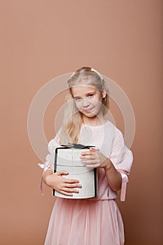 Beautiful blonde girl in a pink elegant dress holds a gift box decorated with a bow