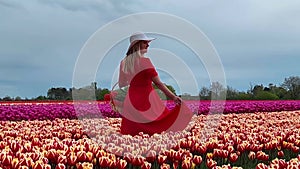 Beautiful blonde girl in red dress and white straw hat with wicker basket on colorful tulip fields