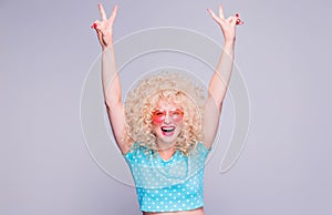 Beautiful blonde girl in retro style with voluminous curly hairstyle in a blue polka-dot blouse and pink glasses on a gray