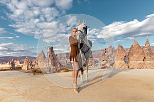 Beautiful blonde girl riding white horse in the mountain desert of Cappadocia in the rays of sunset